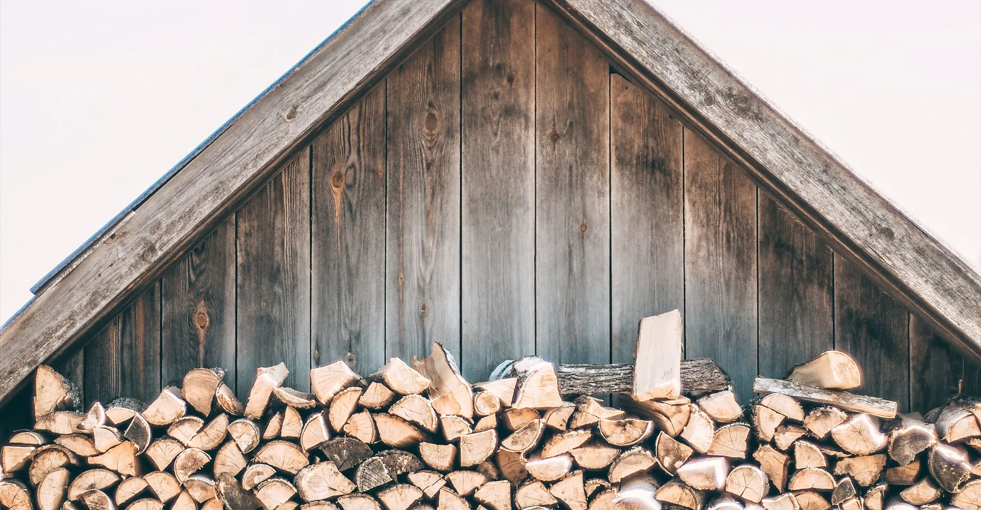 Stacked firewood beneath the timber gable of a wooden house